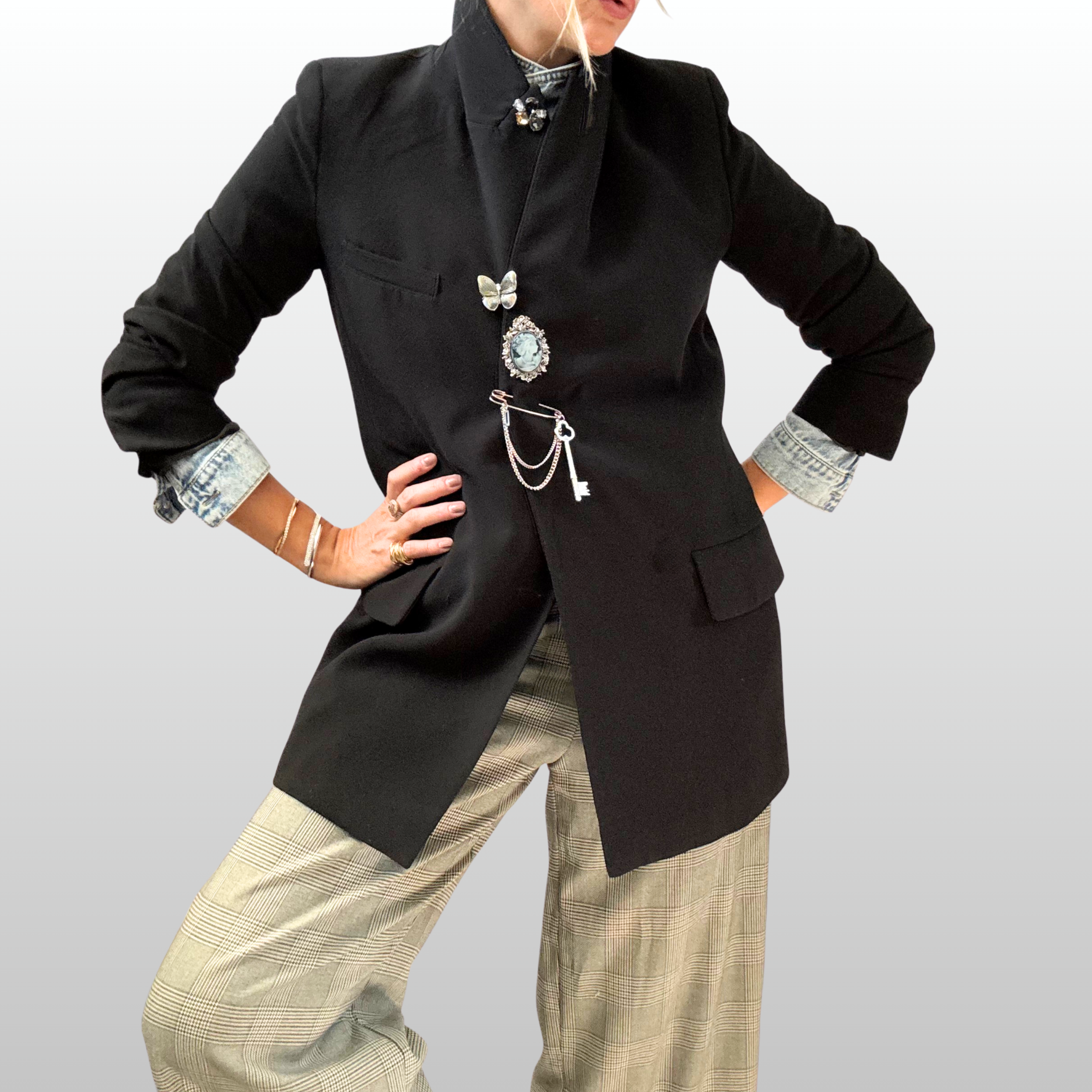 A woman wearing checked trousers and a black blazer. The blazer is secured with a stack of 4 vertical silver tone brooches from The Brooch House.
