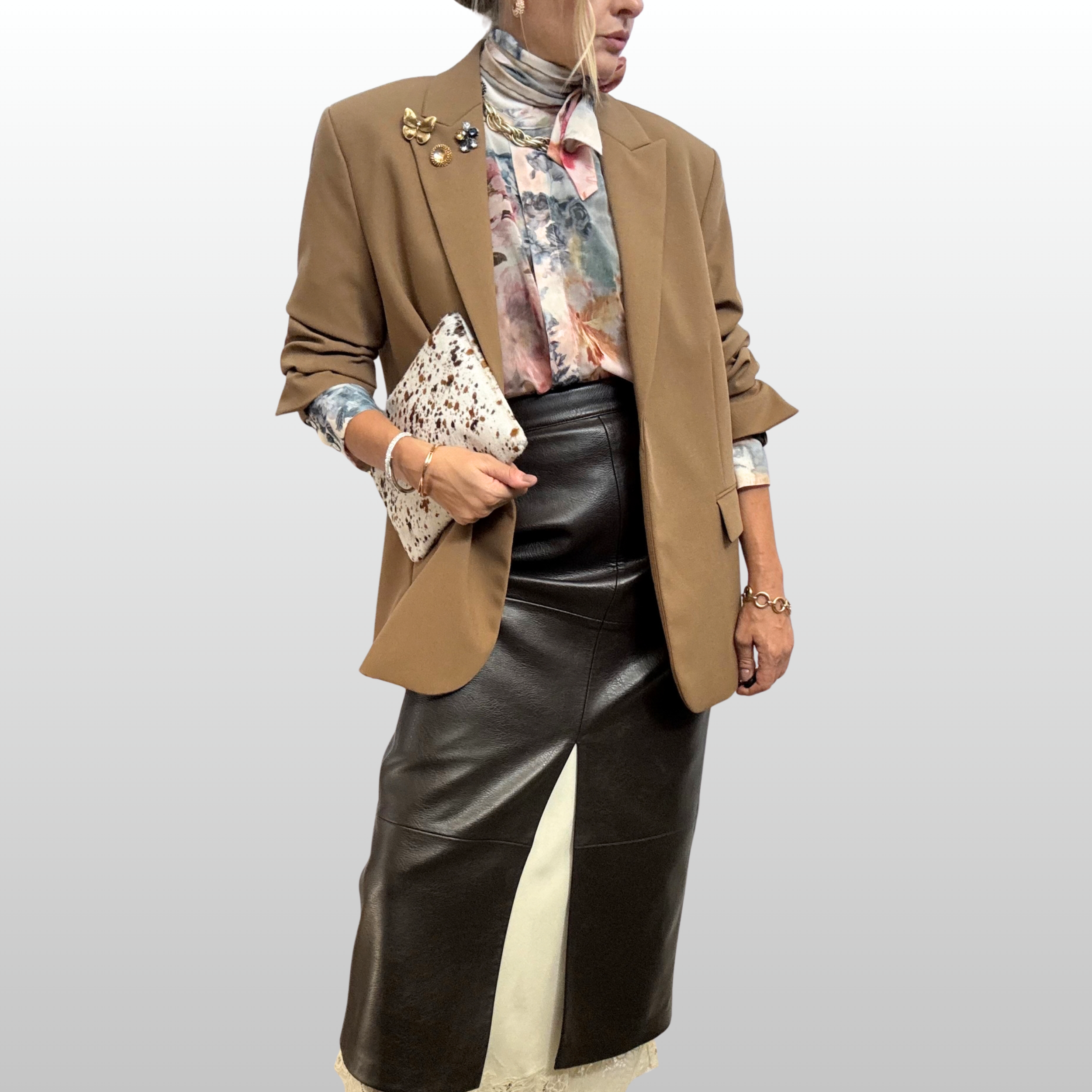 A close up of a woman wearing a sheer floral shirt with a brown leather midi skirt. The looked is topped off with a camel blazer accented with three golden and amber brooches from The Brooch House.