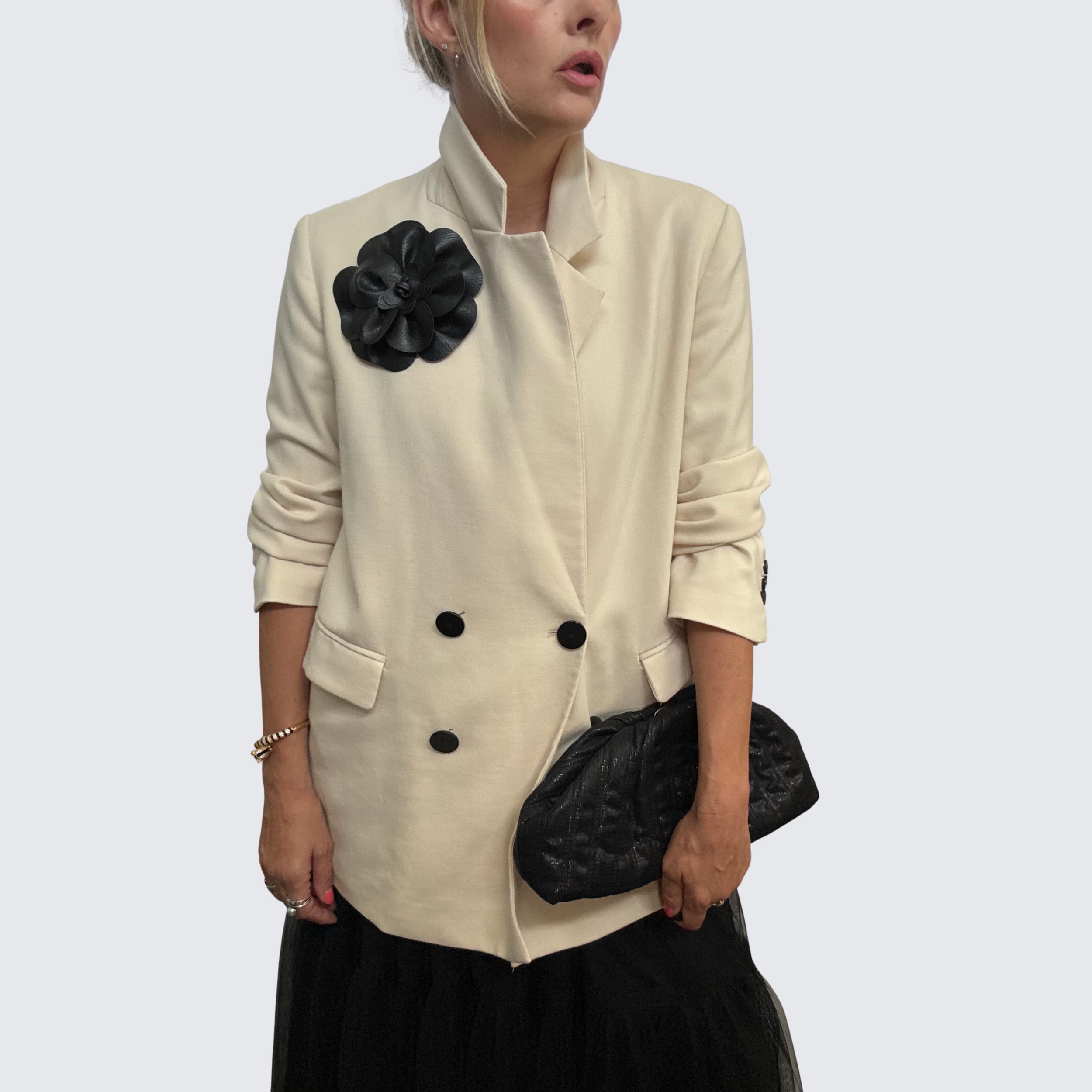 Close-up of woman wearing oversized black leather floral brooch on white blazer.