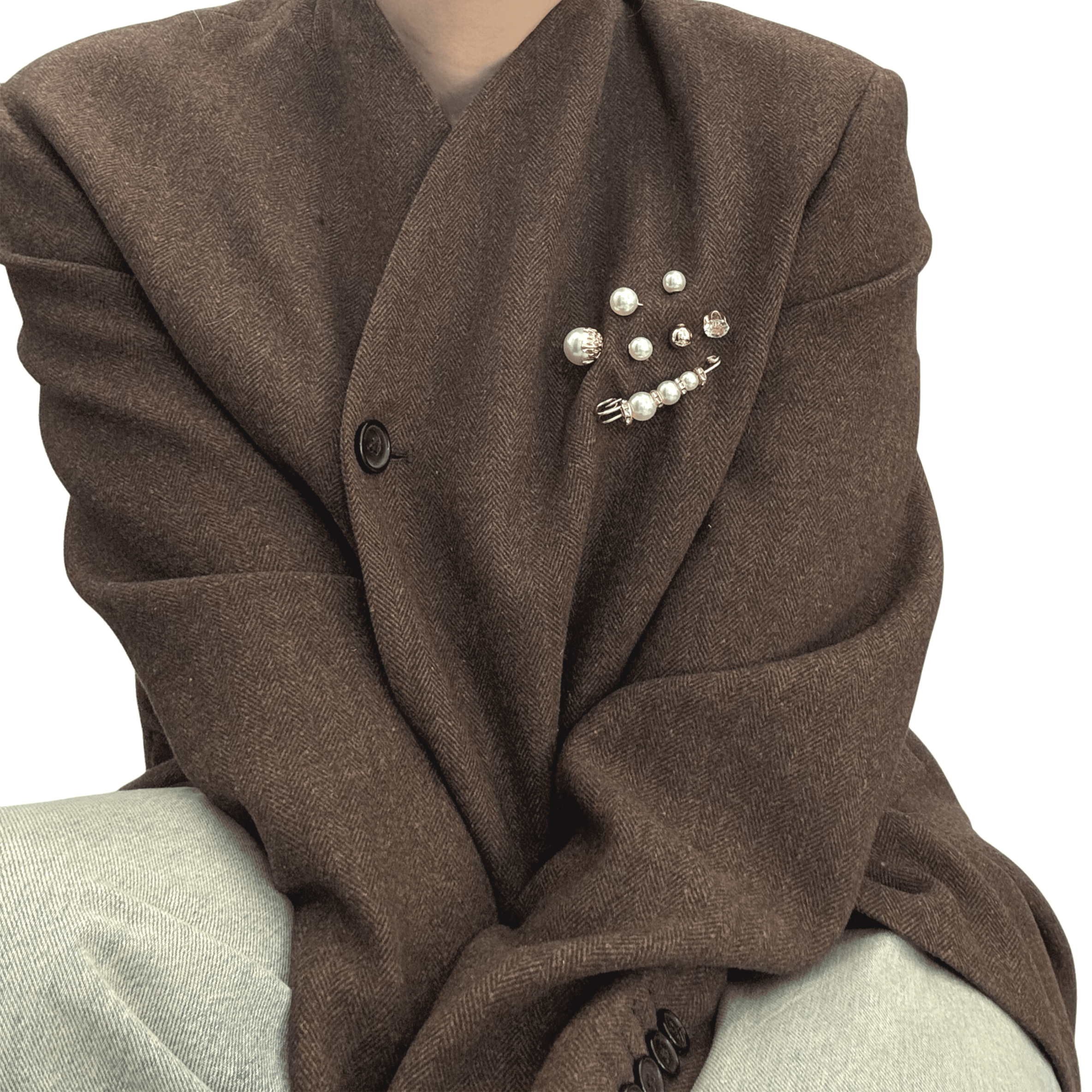 A curated set of five unique pearl pins featuring varied pearl sizes, high-shine gold-toned settings, and subtle crystal accents styled in a cluster on the lapel of a brown wool oversized blazer.