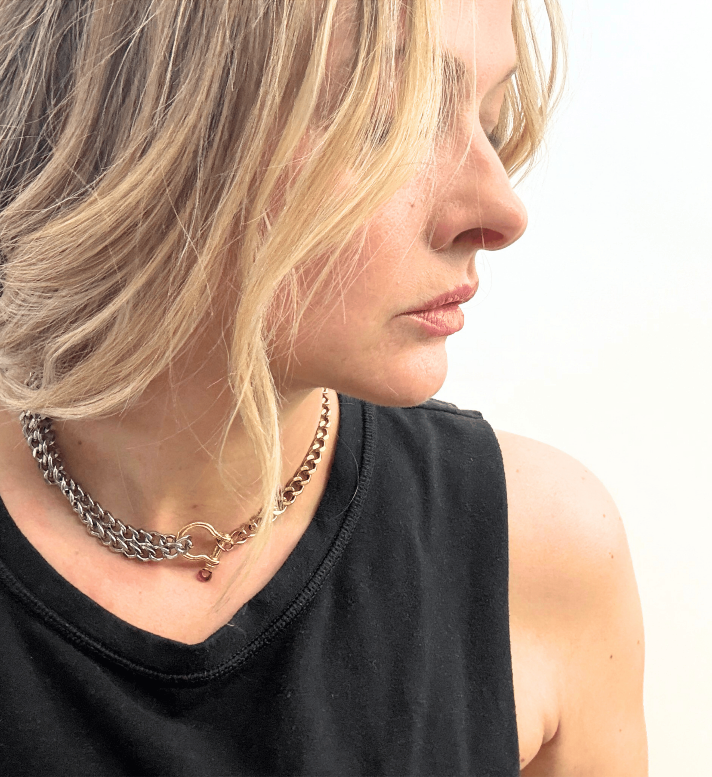 A bold, carabiner-style junction on a substantial, high-shine curb link chain, styled with a classic black tank.