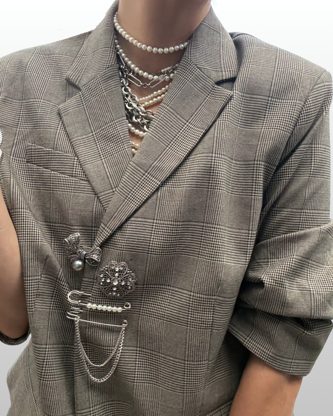 A woman wearing a plaid blazer and pearls and solver jewelry. She also wears a brooch stack featuring a structural mix of silver hardware alongside pearls.