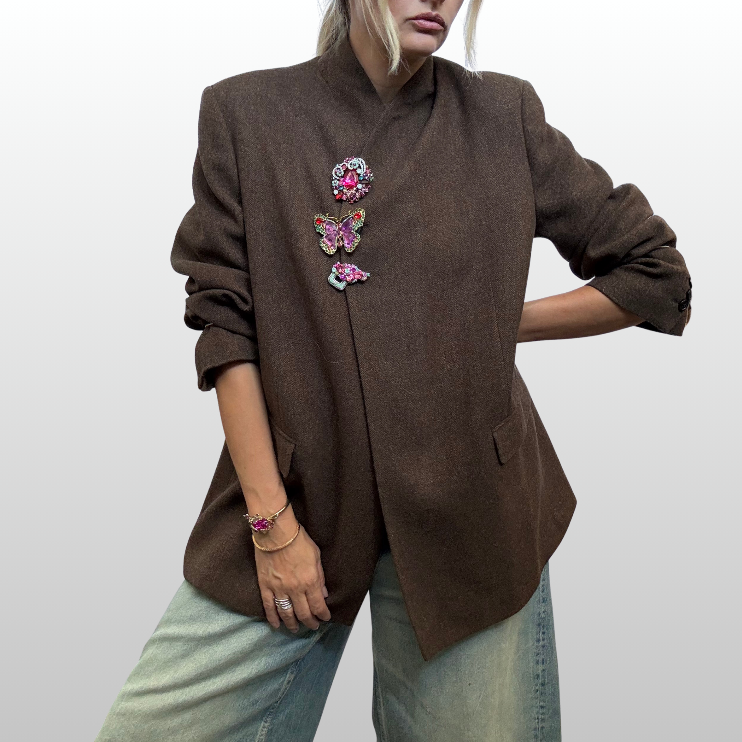 Woman wearing brown blazer with a vertical row of 3 brooches at the closure.  Featuring a purple and green butterfly from The Brooch house at the centre.