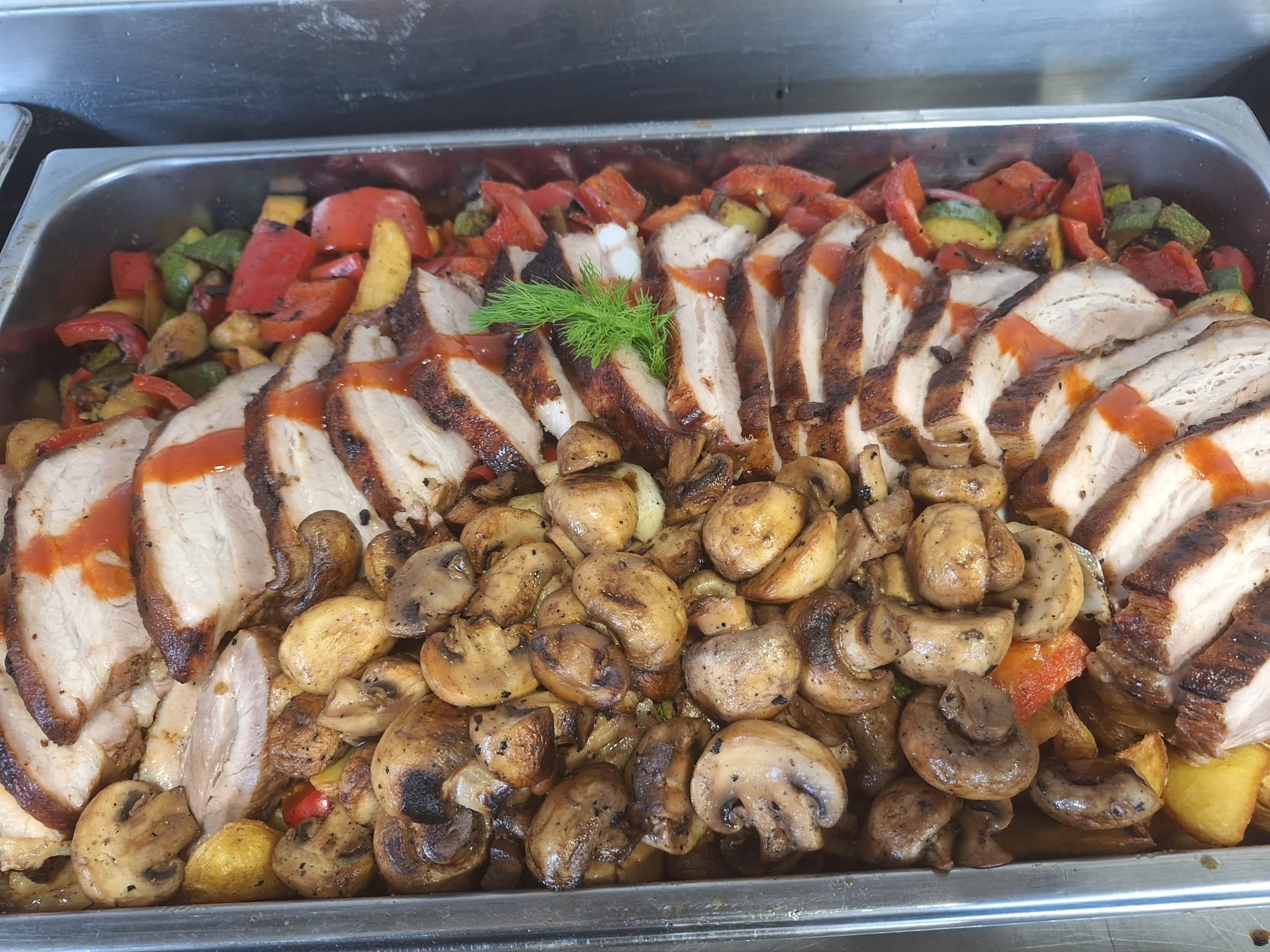 Sliced roasted chicken breast with grilled mushrooms, roasted vegetables, and a sprig of dill on top.