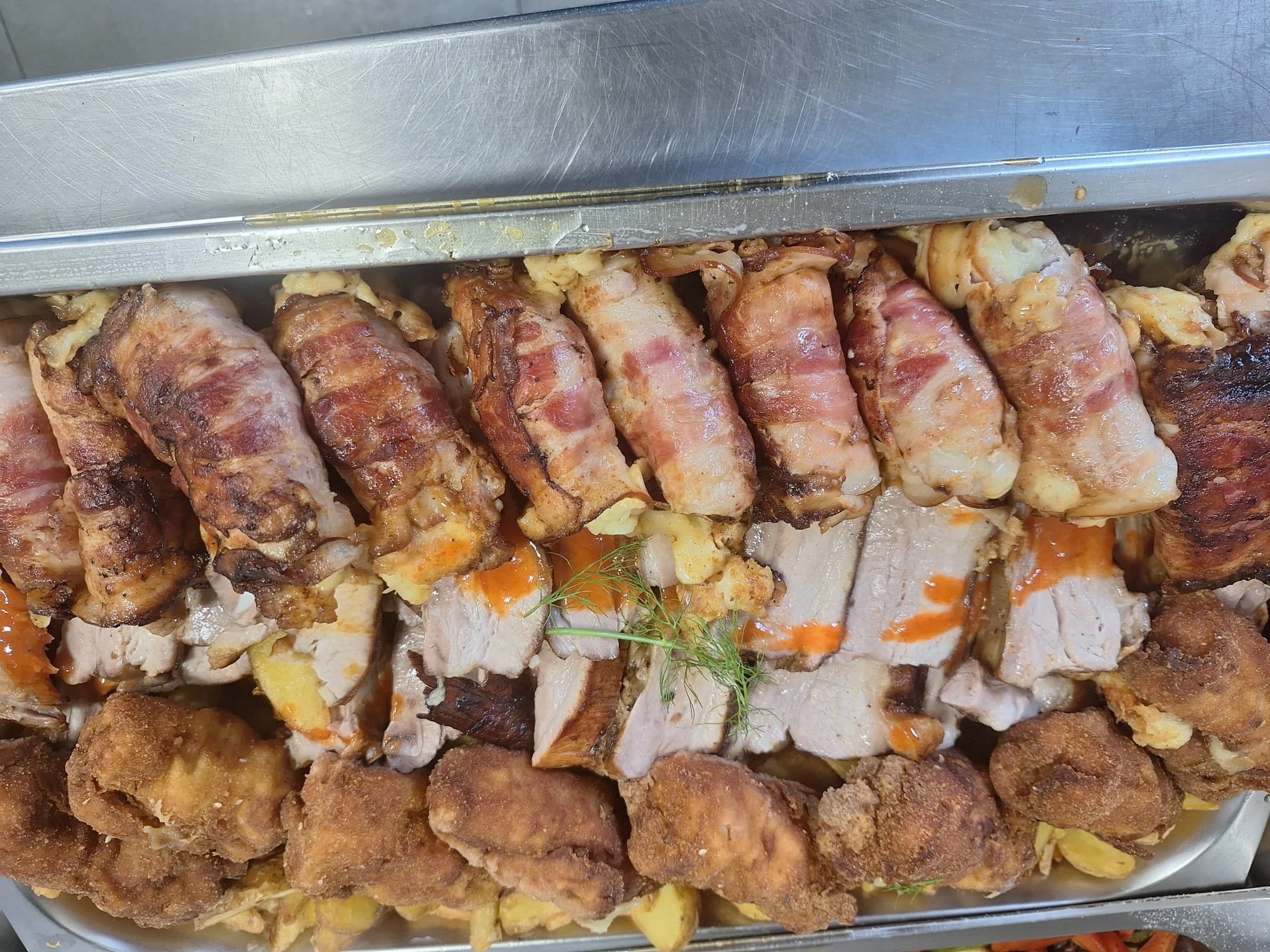 Assorted cooked meats including bacon-wrapped chicken pieces and fried chicken on a metal tray