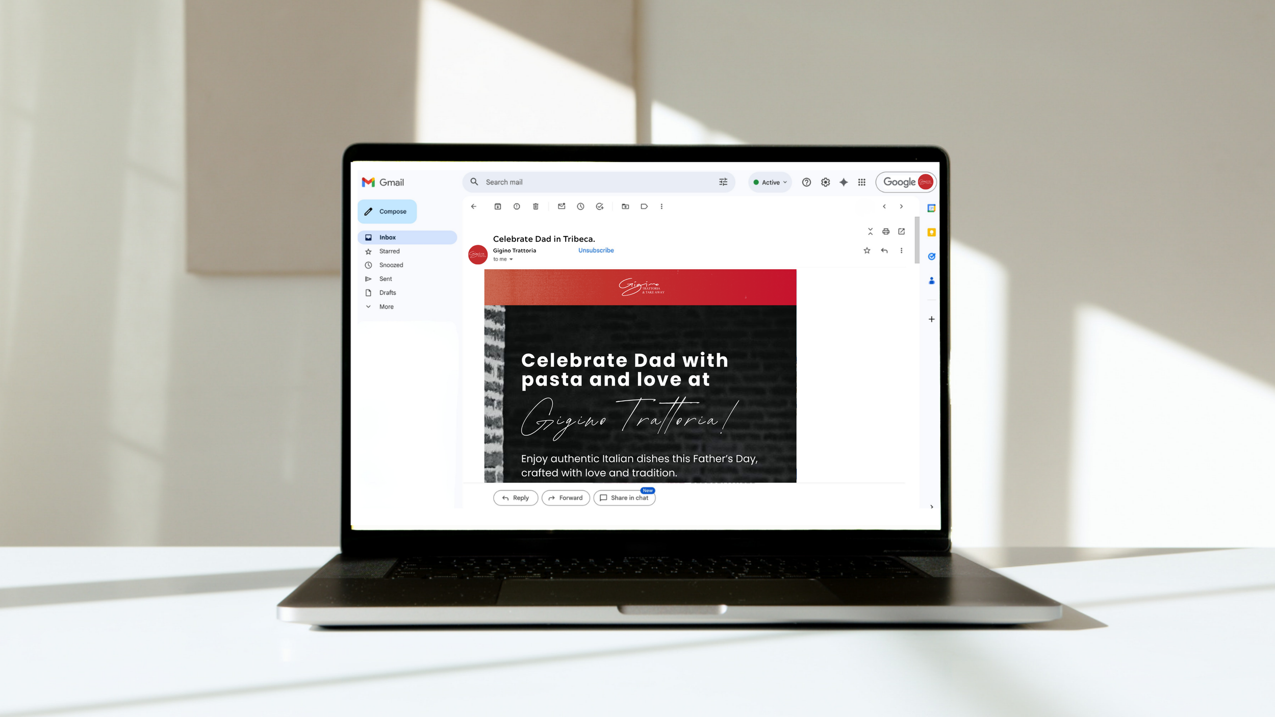 Laptop displaying an email promotion for Father's Day, featuring pasta dishes, on a white desk with sunlight and shadows in the background.