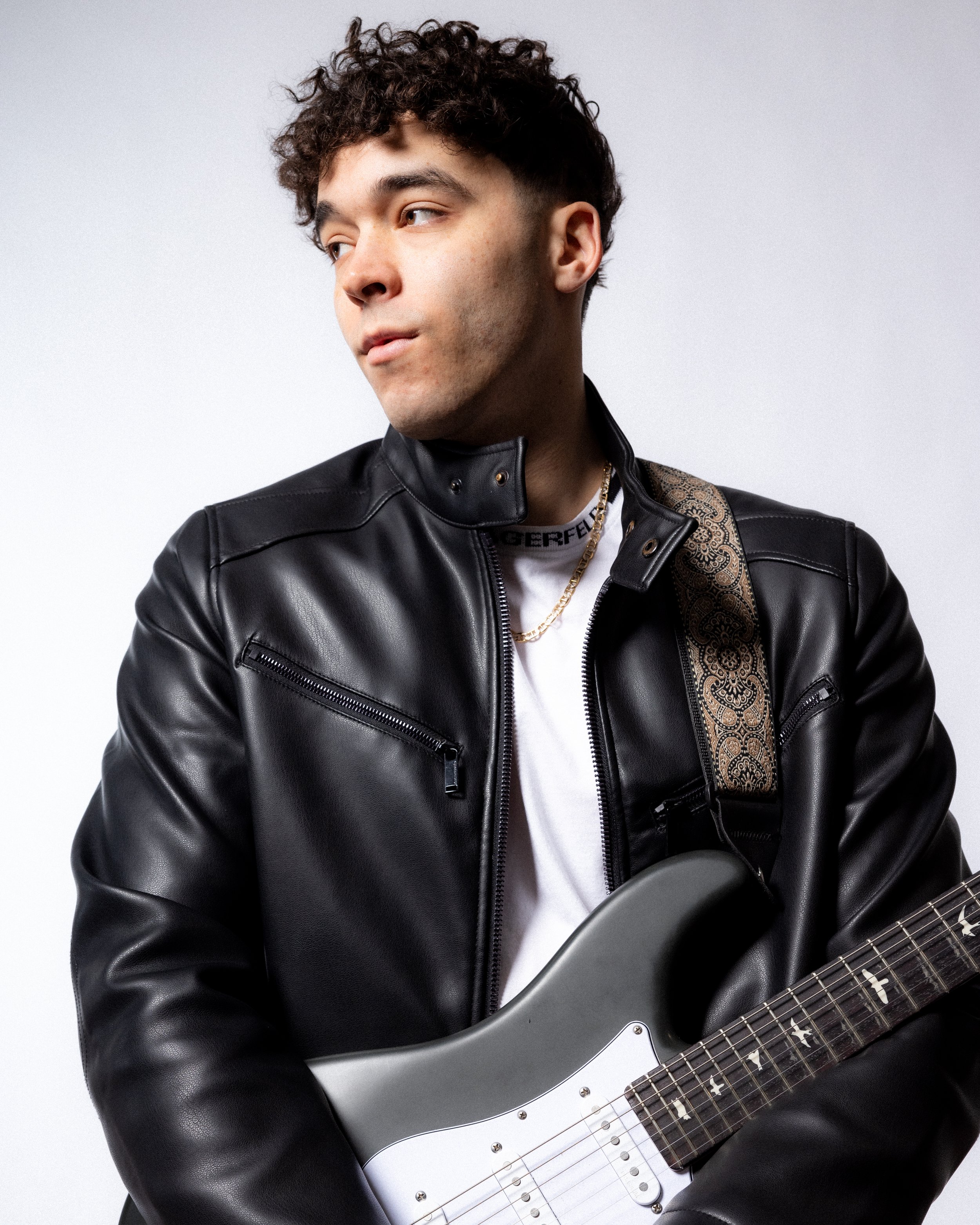 Person posing in front of a red backdrop, wearing a white sports jersey with a black logo and black pants.