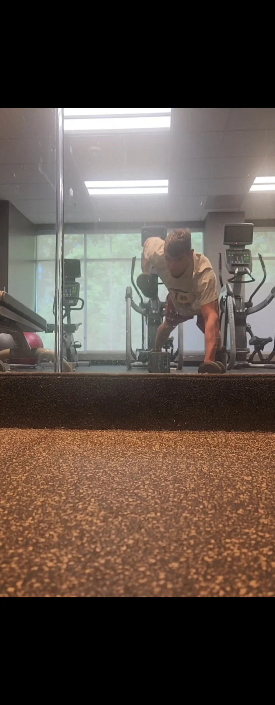 Person doing a plank exercise at a gym, viewed through a mirror.