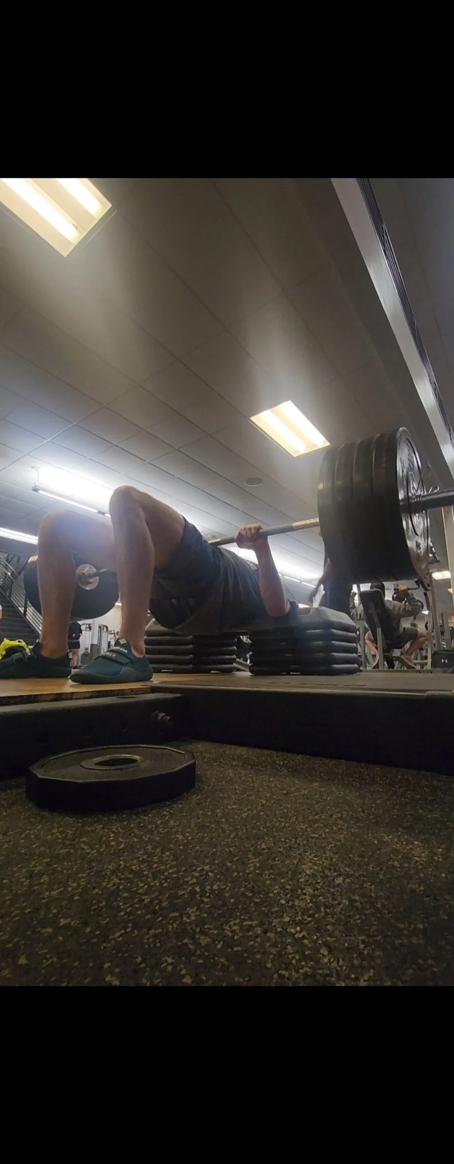 A man performing a bench press exercise with a barbell loaded with large weights at a gym. He is lying on a bench, with his feet flat on the ground, and in a slightly bent position.