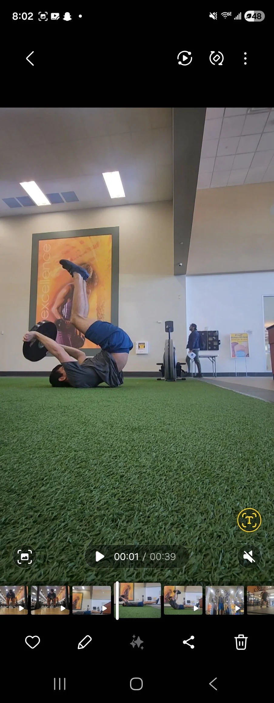 A person doing a reverse crunch exercise on a green artificial turf in a gym, holding a weight plate with their knees bent and feet in the air.