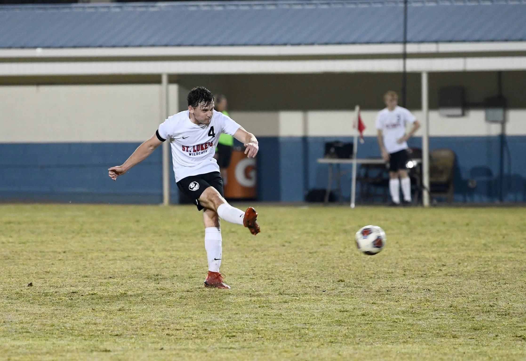 Soccer player preparing to kick the ball on the field with a teammate in the background.