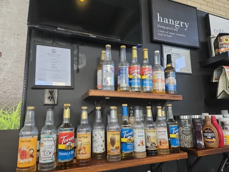 Display of flavored syrups and bottles, with a sign reading 'hangry' above them.