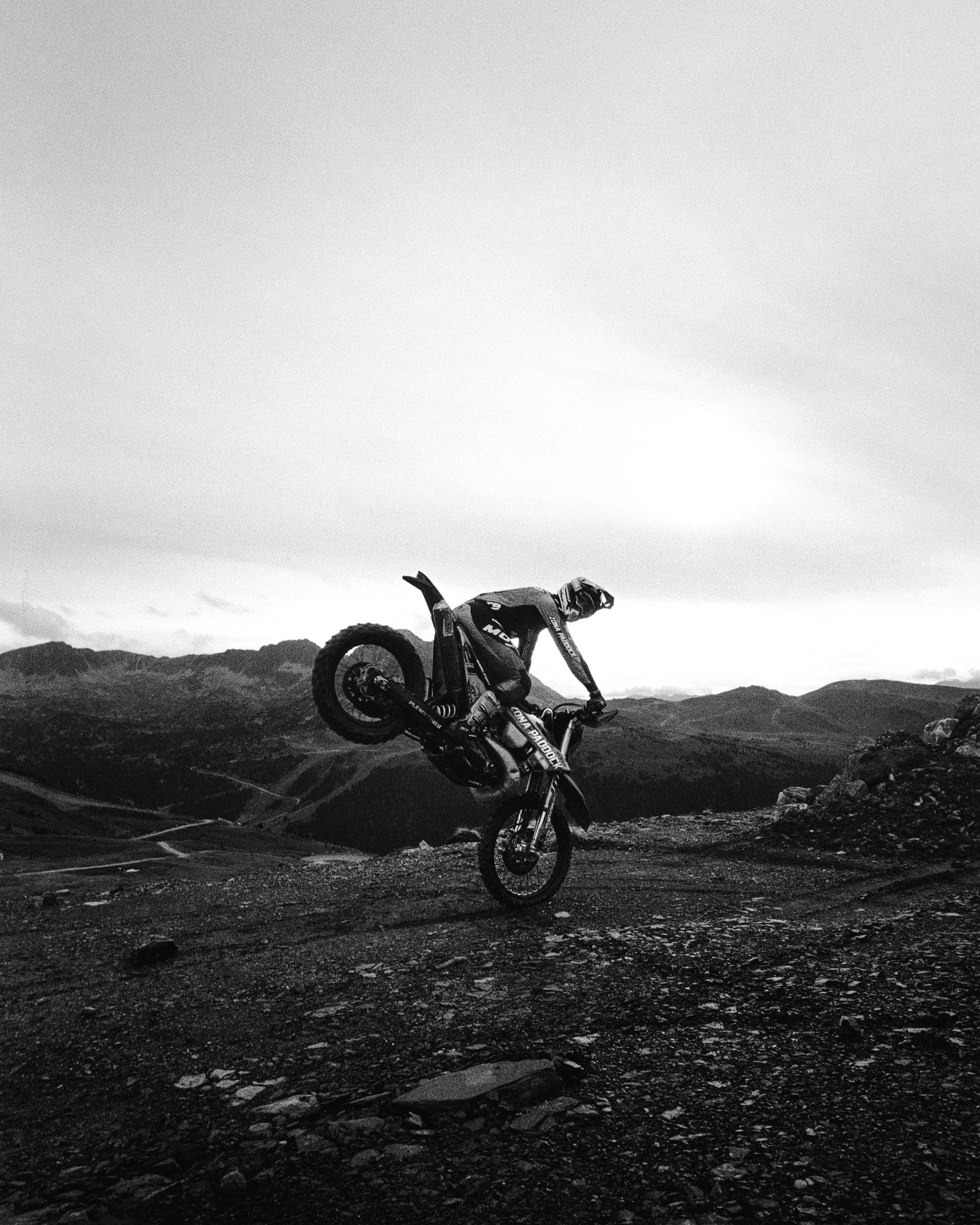 Un motociclista realiza un truco de salto en un paisaje montañoso en blanco y negro.