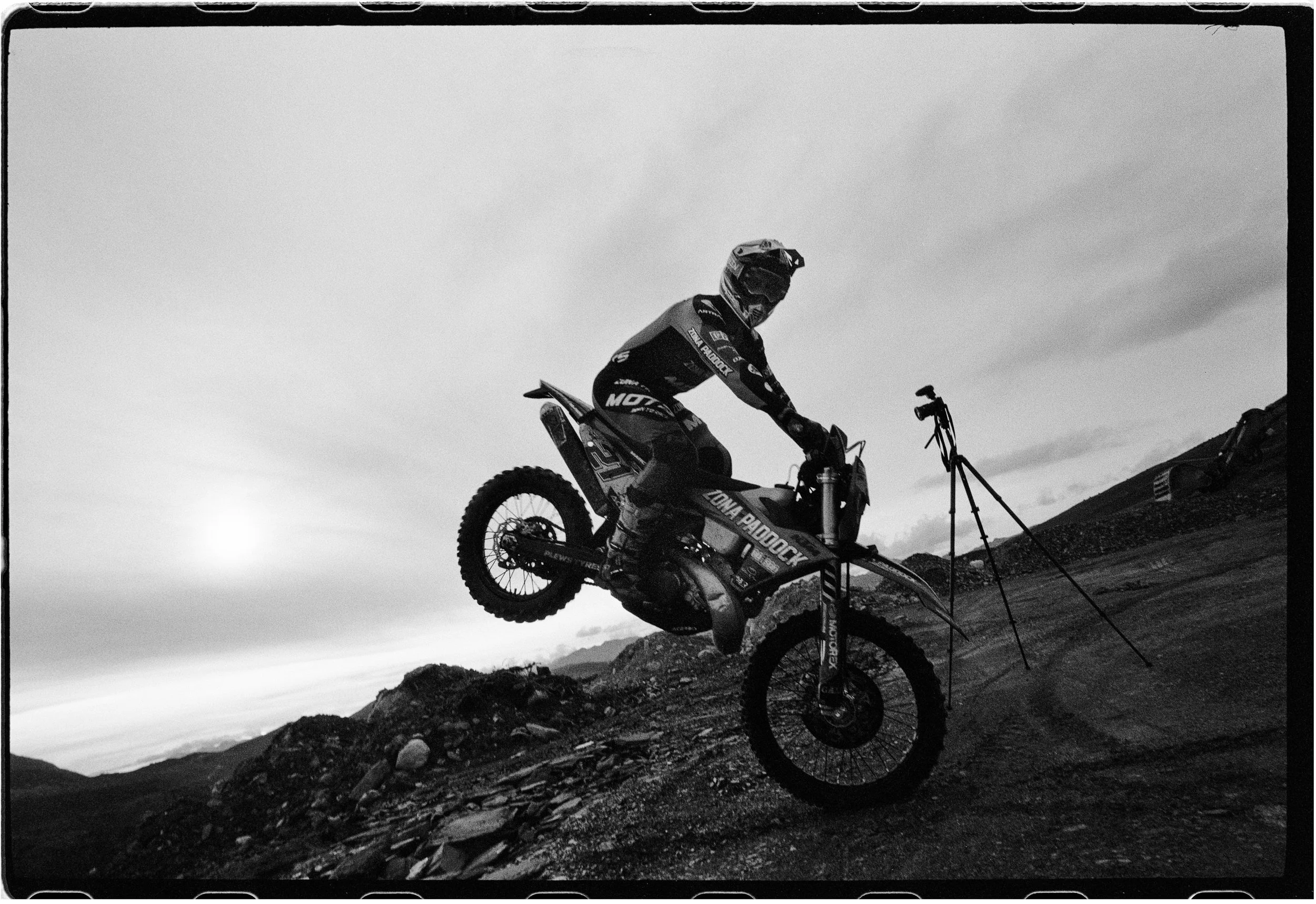 Una motocicleta de enduro saltando en un terreno de montaña al atardecer.