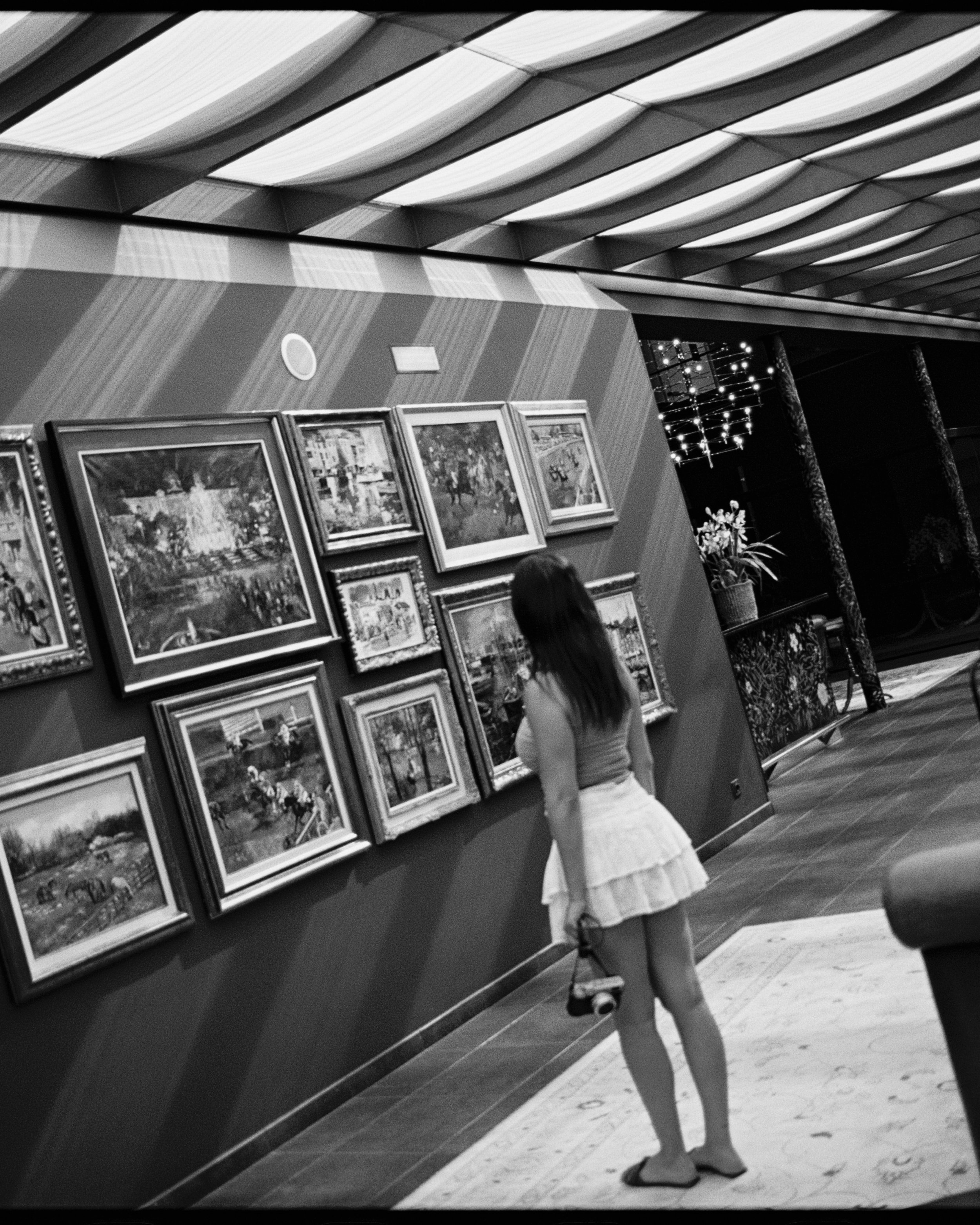 Joven mujer observando cuadros en una galería de arte en un espacio interior con iluminación moderna y decoración