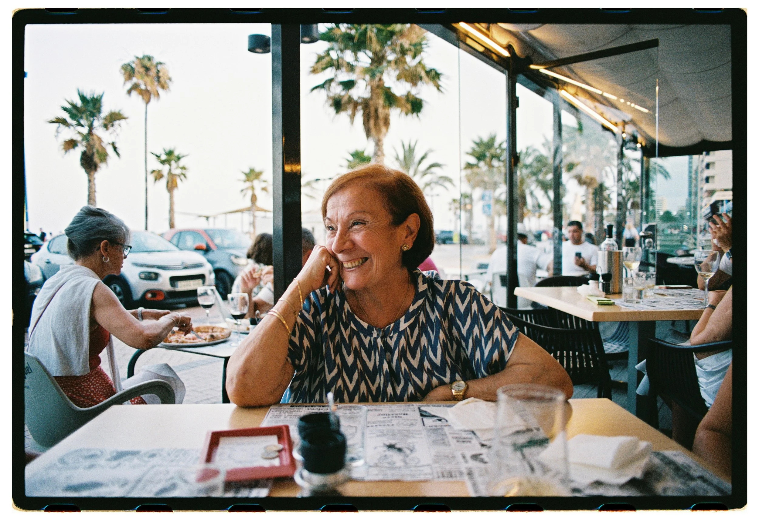 Mujer sonriendo en un restaurante con vista a la calle y palmeras