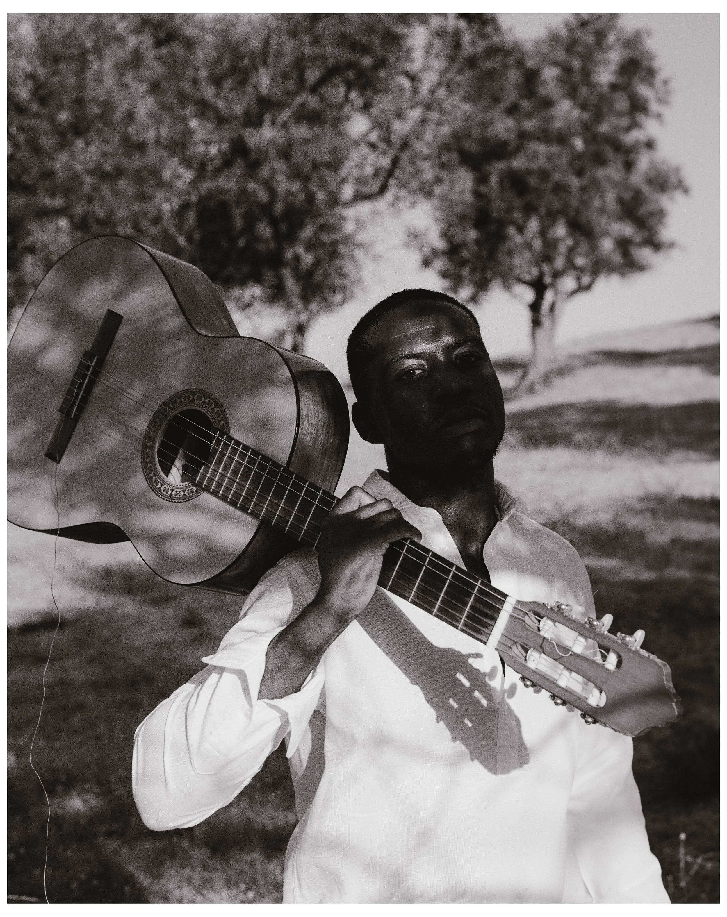 Hombre con guitarra en un campo, en blanco y negro.