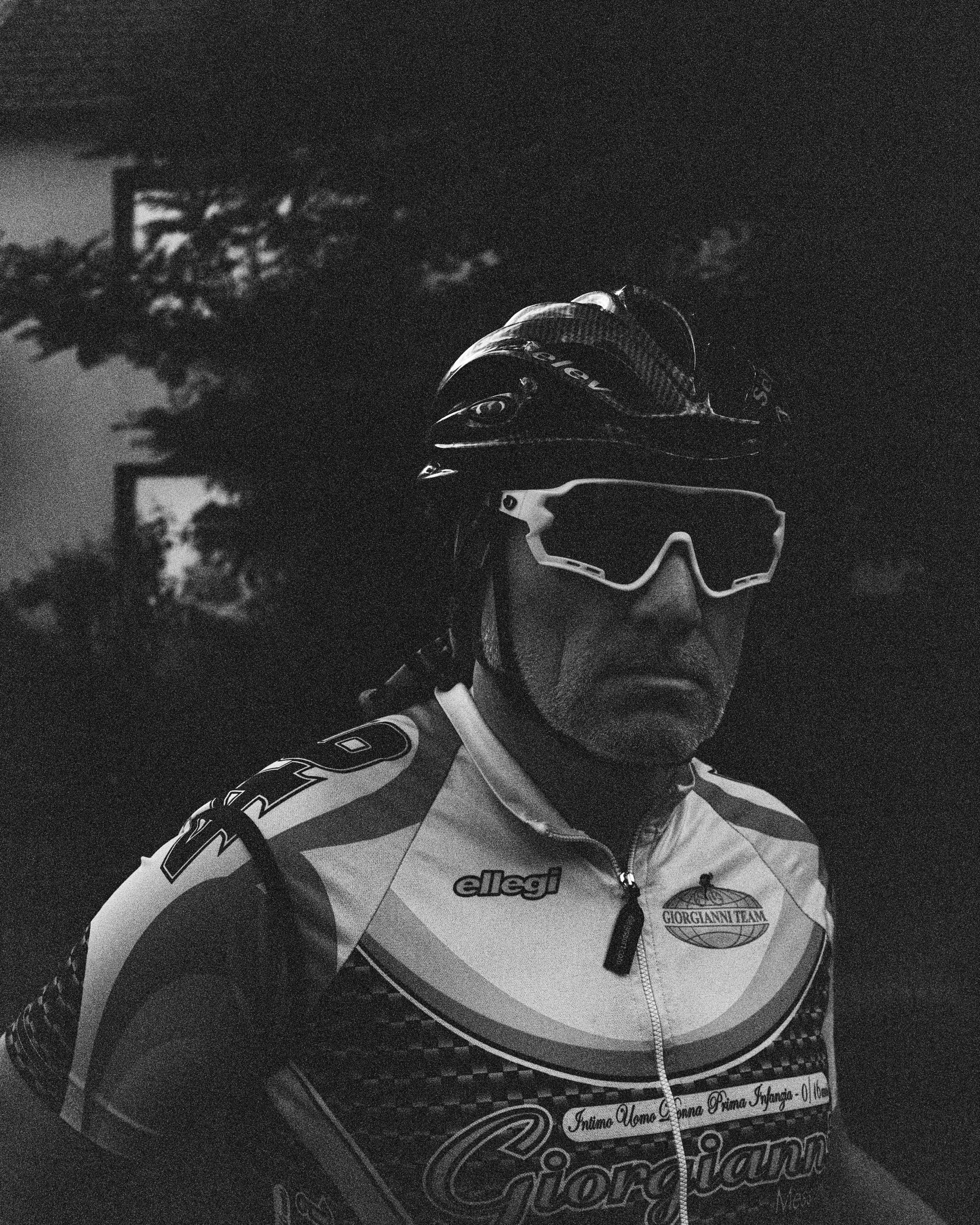 Hombre con casco y gafas de protección, vestido con uniforme de ciclismo, en un entorno oscuro y urbano.
