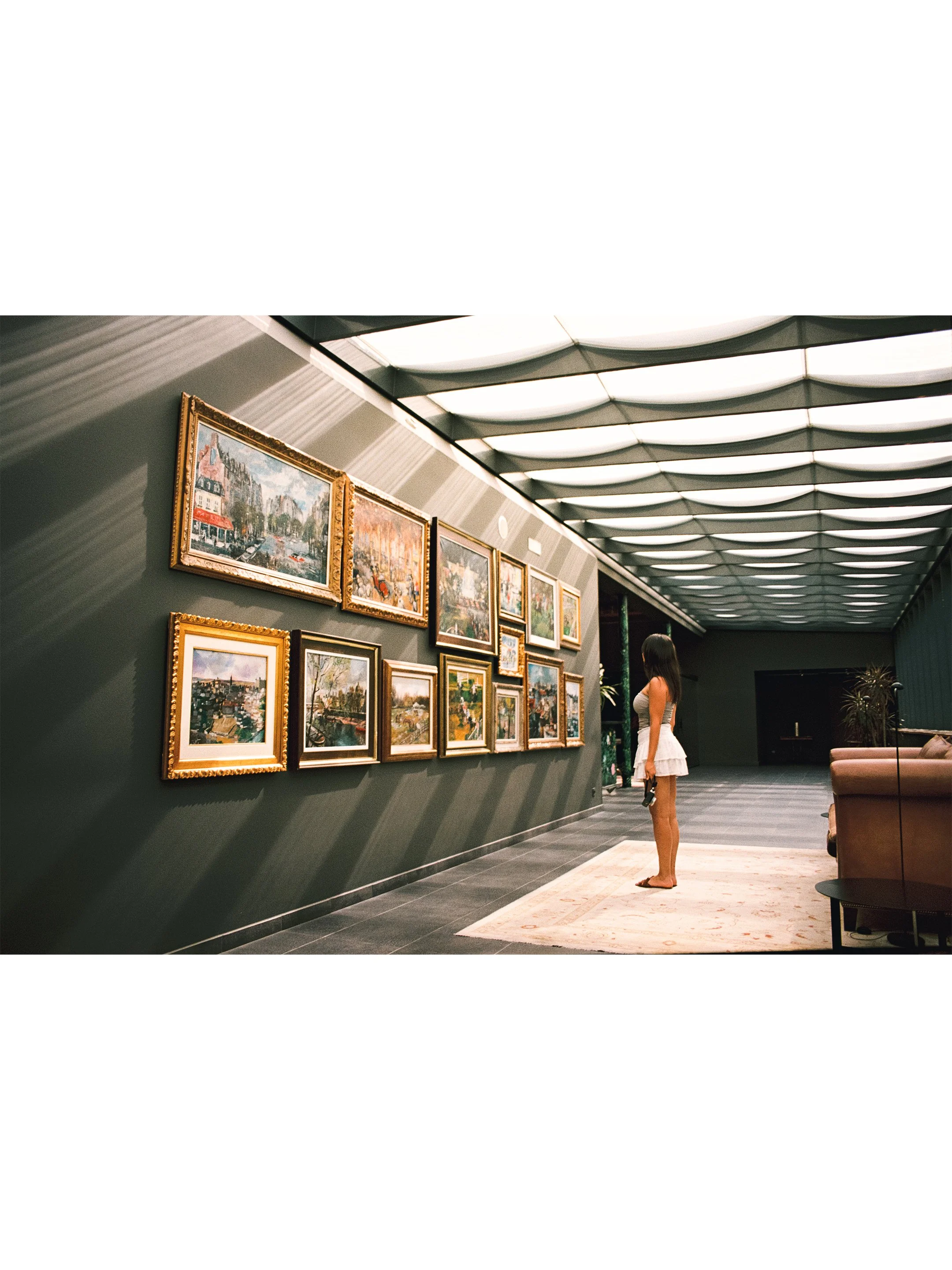 Mujer observando pinturas en una galería de arte con paredes verdes y techo con estructura de ondas.