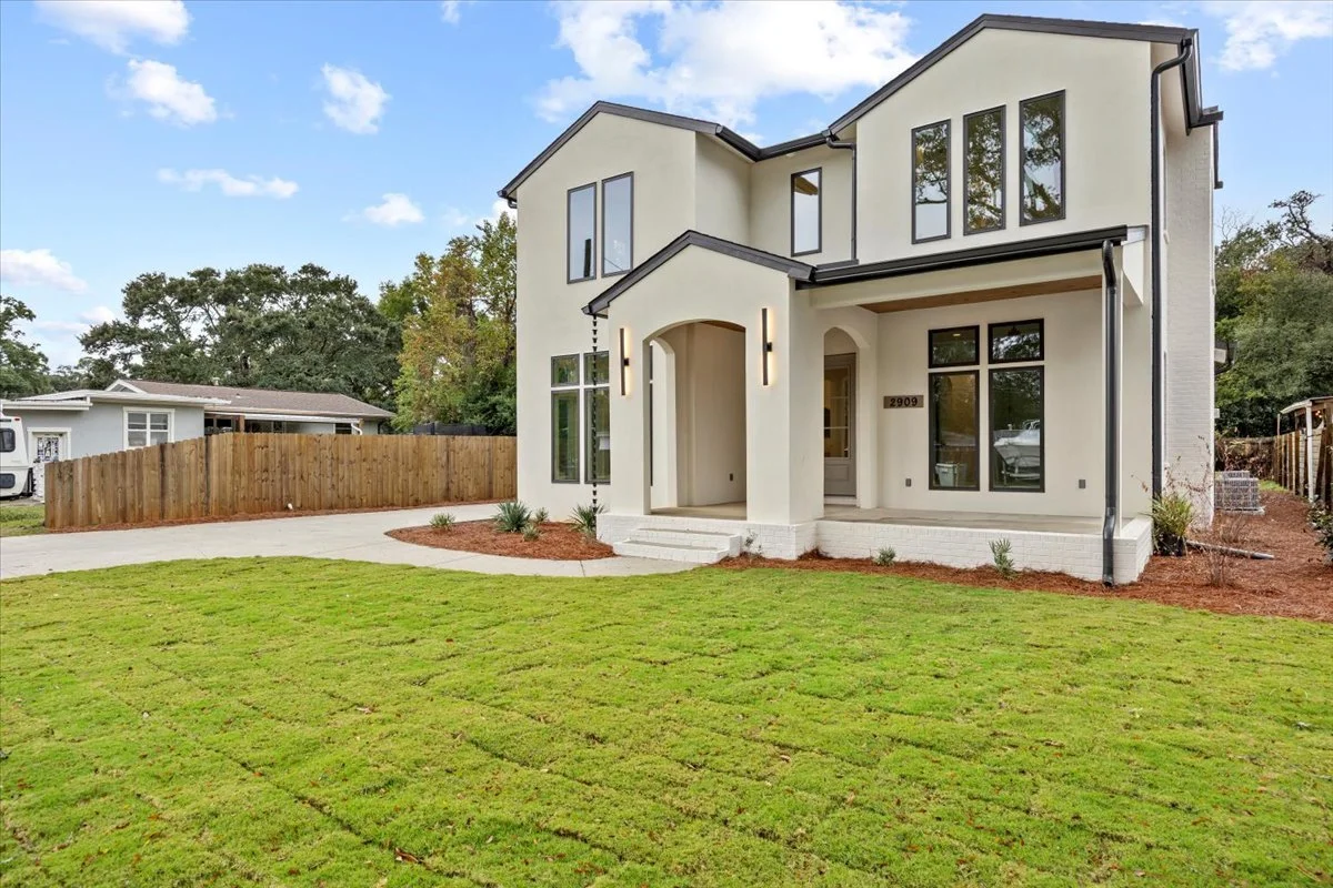 New two-story house with a white exterior, black trim, and large windows, surrounded by a green lawn and a wooden fence.
