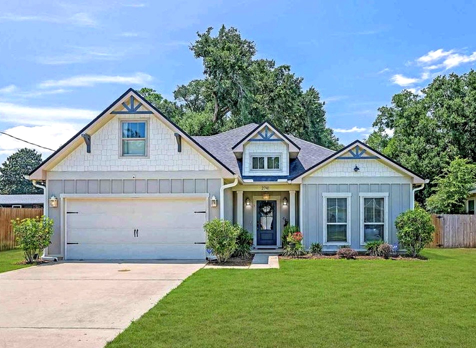 Front view of a modern suburban house with a two-car garage, manicured lawn, and landscaped garden, under a blue sky with some clouds.
