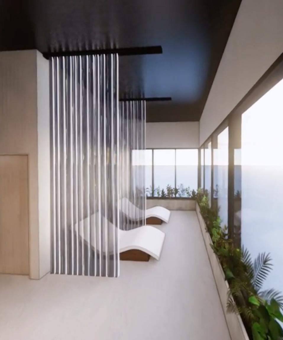 Balcony with two white lounge chairs, glass windows showing a view of the ocean, and green plants along the edge.