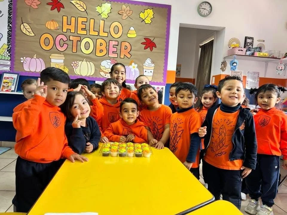 Niños en una clase de preescolar celebrando octubre con decoraciones de otoño y postres en la mesa.
