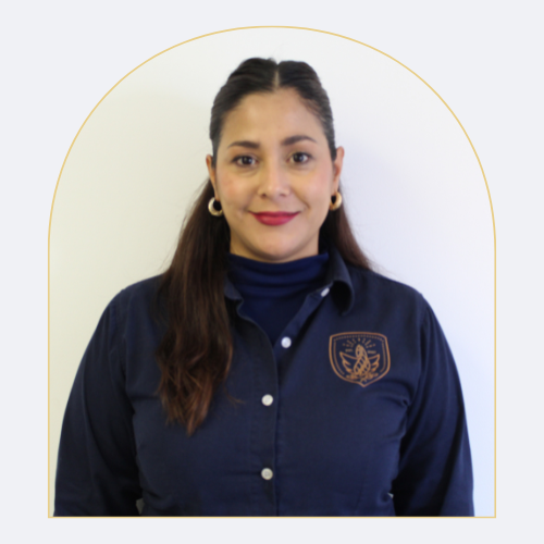Retrato de una mujer con cabello castaño oscuro, usando una camisa azul con un logotipo y un suéter azul debajo, sonriendo frente a un fondo blanco con un círculo dorado.