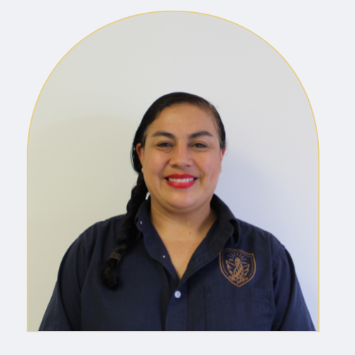 Mujer sonriendo, con cabello recogido en trenza, usando uniforme oscuro con escudo en el pecho, fondo blanco.