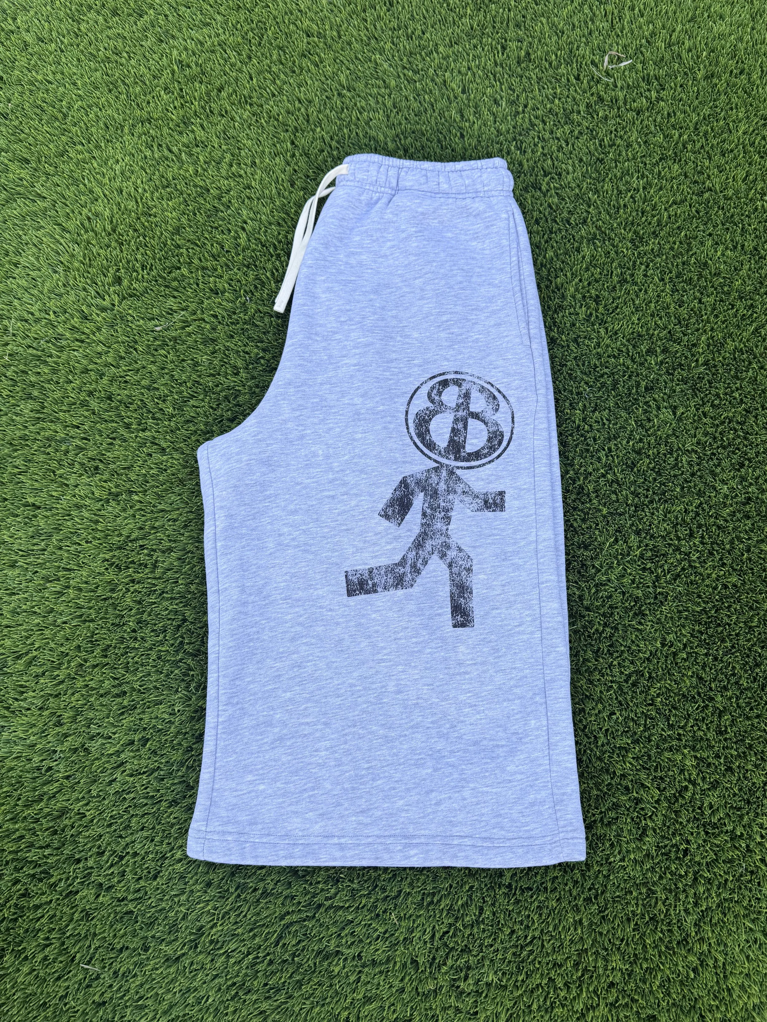 A pair of gray sweatpants with a black Darth Vader logo on the left leg, lying on green grass.