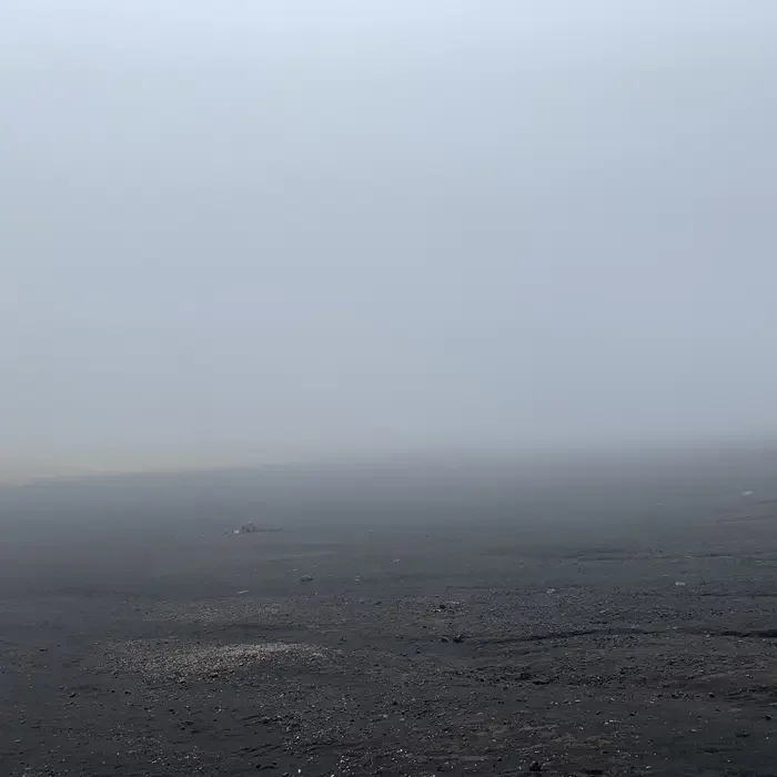 A foggy landscape with a dark, rocky ground and a thick fog obscuring the background.