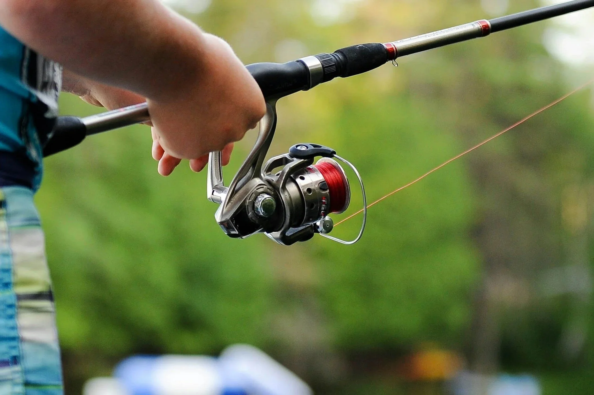 A person holding a fishing rod with a spinning reel, casting a line into a body of water.