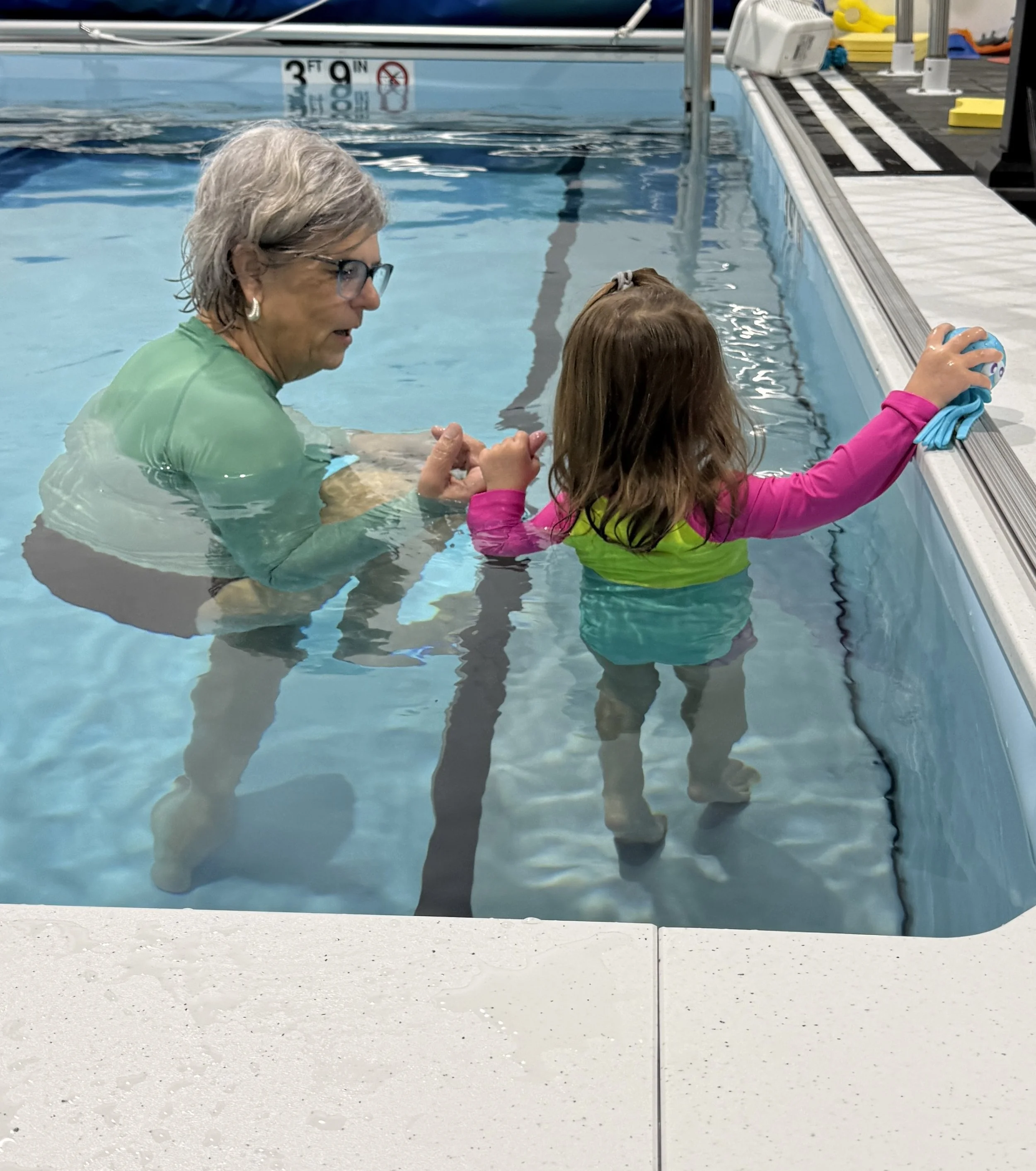 Cathy Sheafor holding girl's hands as the girl reaches out with a small blue toy in her hand. 