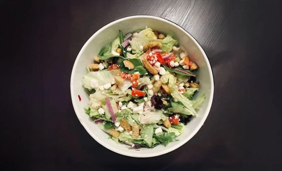 A bowl of salad containing lettuce, cherry tomatoes, red onions, shredded cheese, croutons, and chopped vegetables.