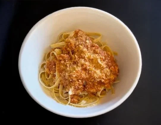 Balanced meal for sustainable nutrition plan. Bowl of cooked spaghetti pasta topped with marinara sauce and grated cheese.
