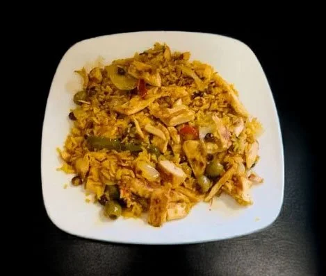 Plate of yellow rice with chicken and vegetables on a white square dish.