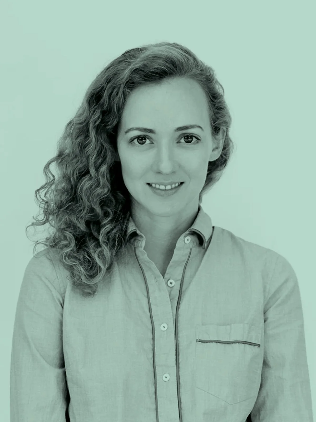 Courtney Eckersley; A woman with long curly hair smiling, wearing a light-colored collared shirt against a plain background.