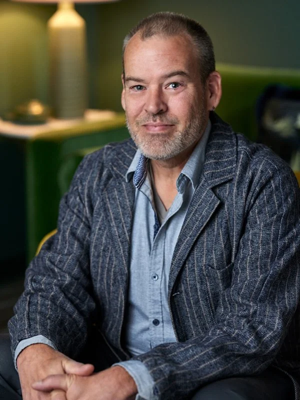 Scott Brannon; A man with a beard and short hair sitting in a room with green walls, wearing a blue shirt and a pinstripe blazer, looking at the camera.