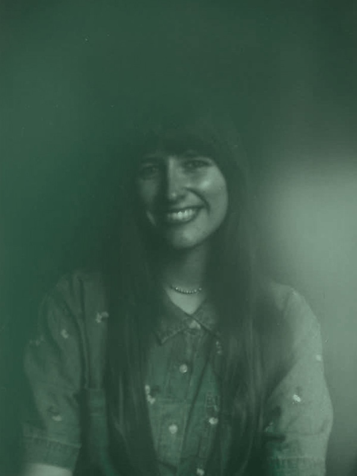 Abbey Marcel; Black and white photo of smiling woman with curly hair, wearing a patterned shirt and necklace, with a soft light on the right side.