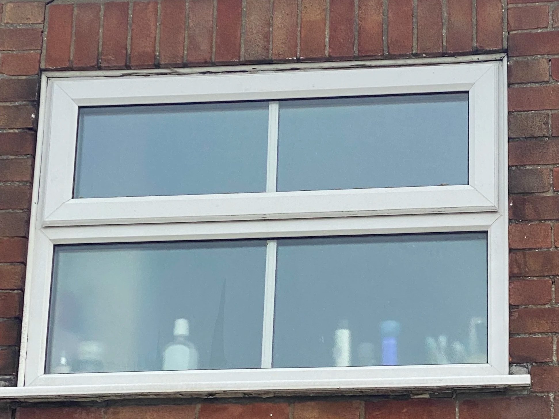 A close-up view of an outdoor rectangular window with a white frame set in a red brick wall.