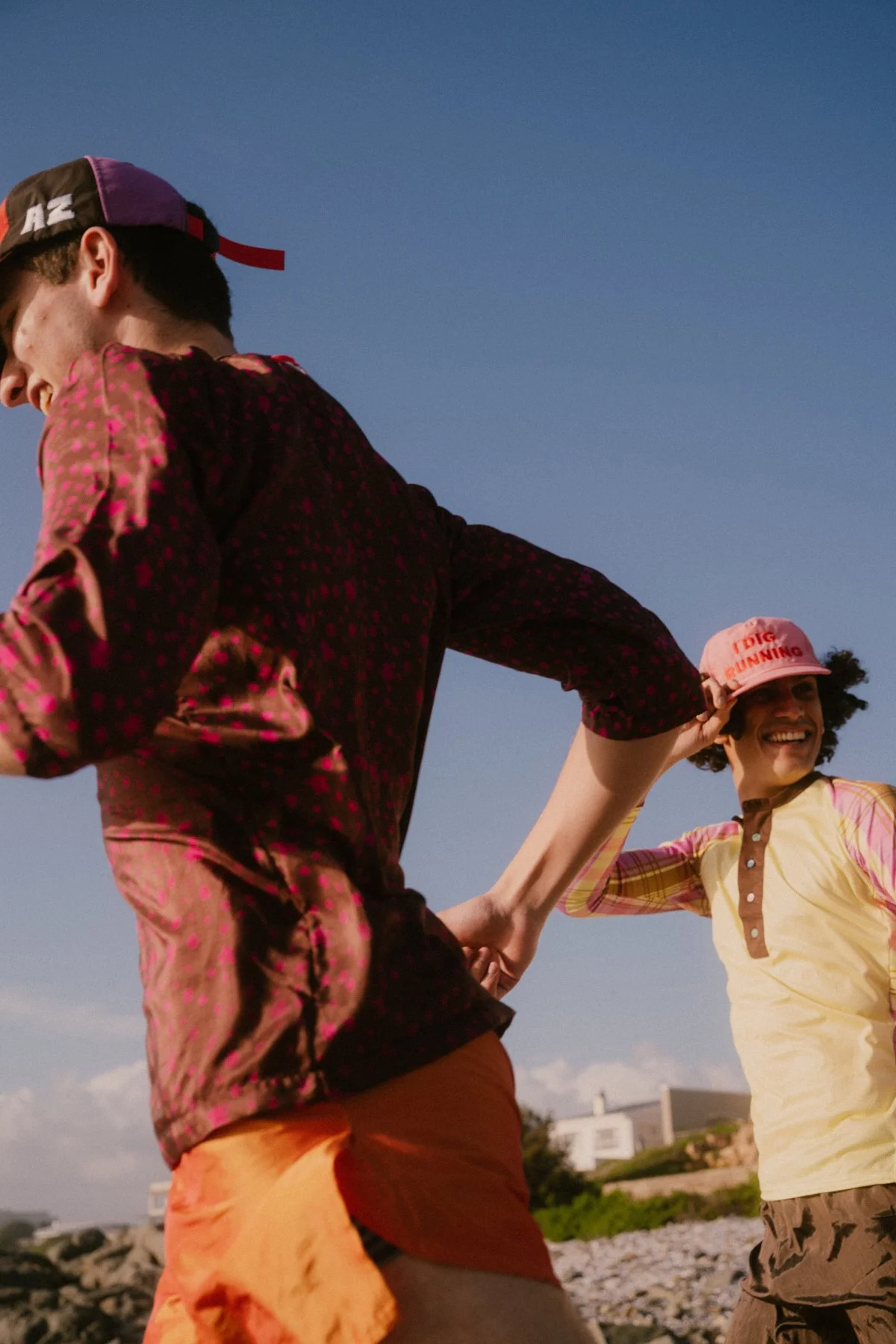 Two friends enjoying a day outdoors on a sunny beach, holding hands and smiling.