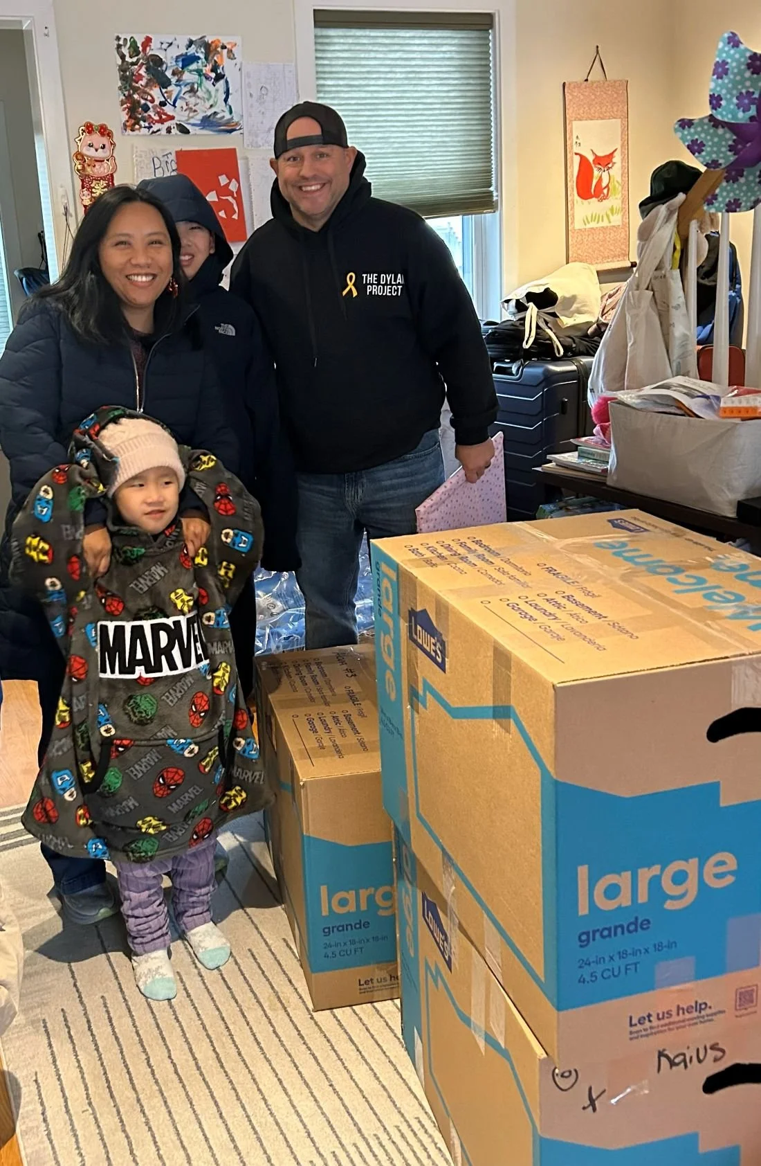 Four people, including a child, standing behind large moving boxes inside a room with decorations and furniture, smiling for the photo.