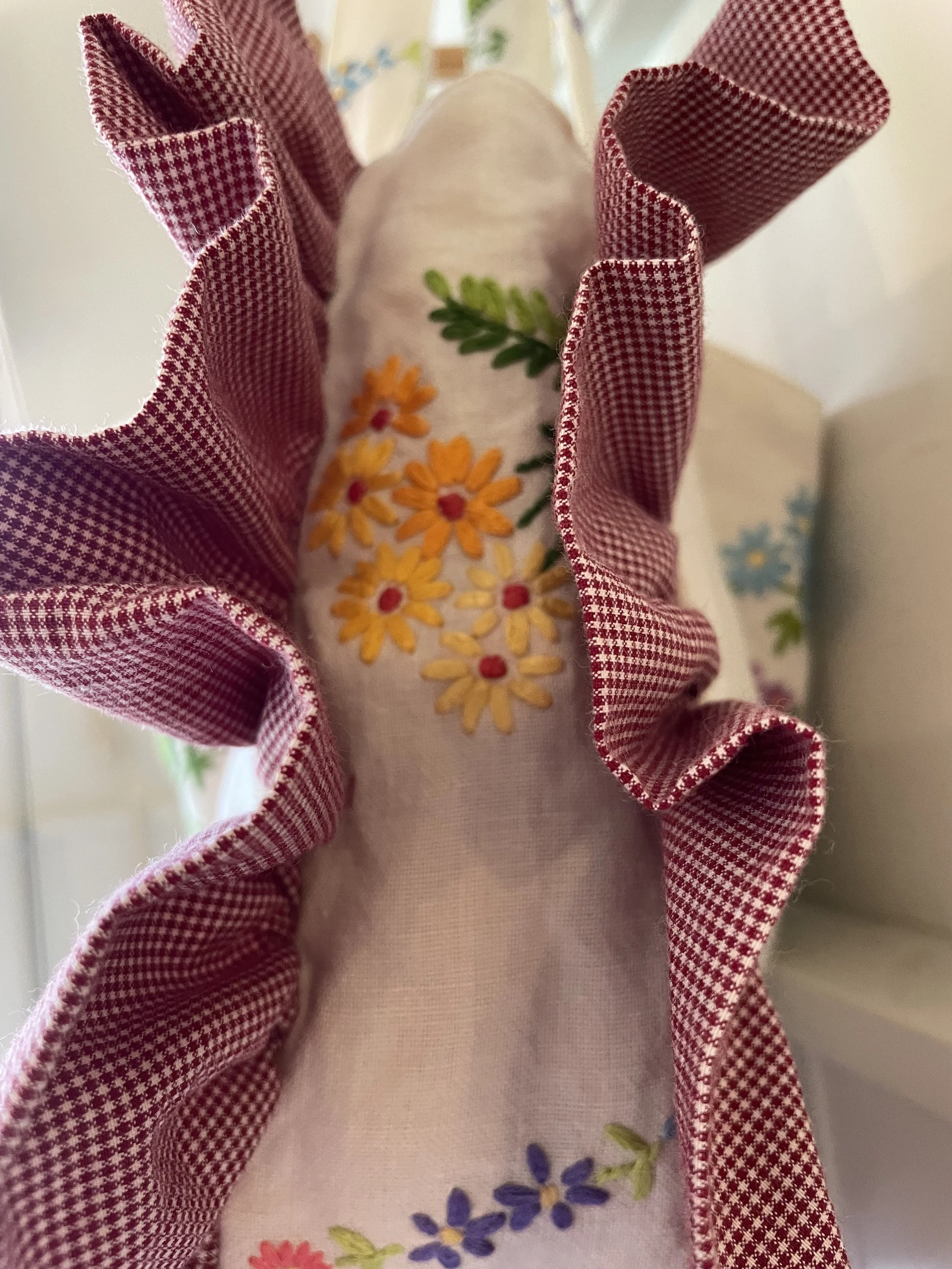 Close-up of a fabric item with embroidered yellow, purple, and red flowers, surrounded by a ruffled red and white checkered fabric.