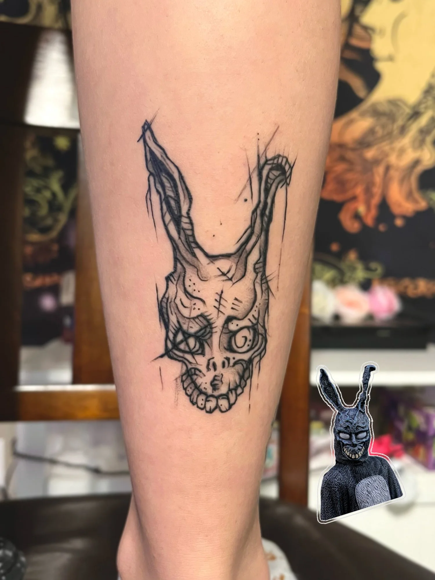 Black ink tattoo of a stylized, abstract skull with elongated, twisted ears on person's forearm.