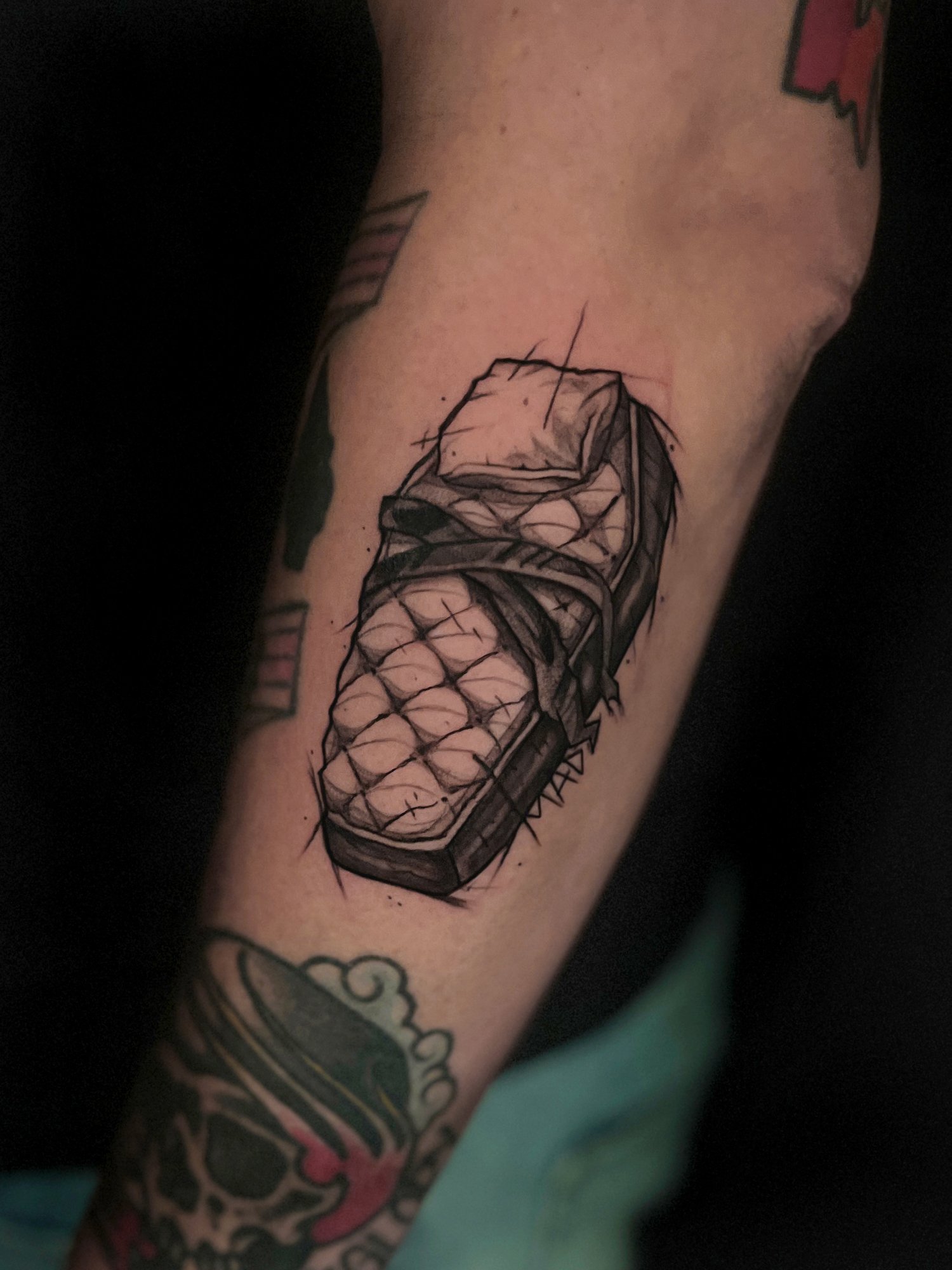 Black and gray tattoo of a bundle of pills in a pillbox on person's forearm.