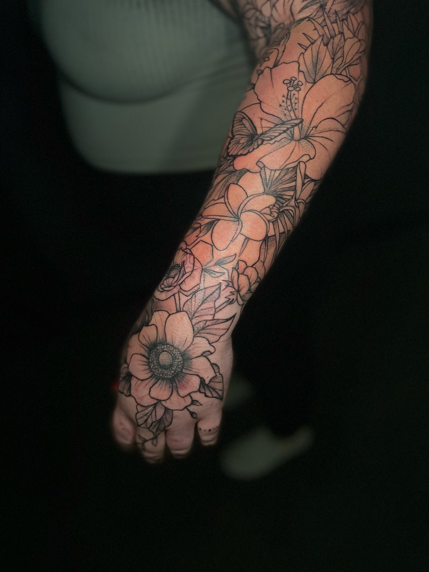 A person's arm with a detailed black ink floral tattoo featuring large flowers and leaves.