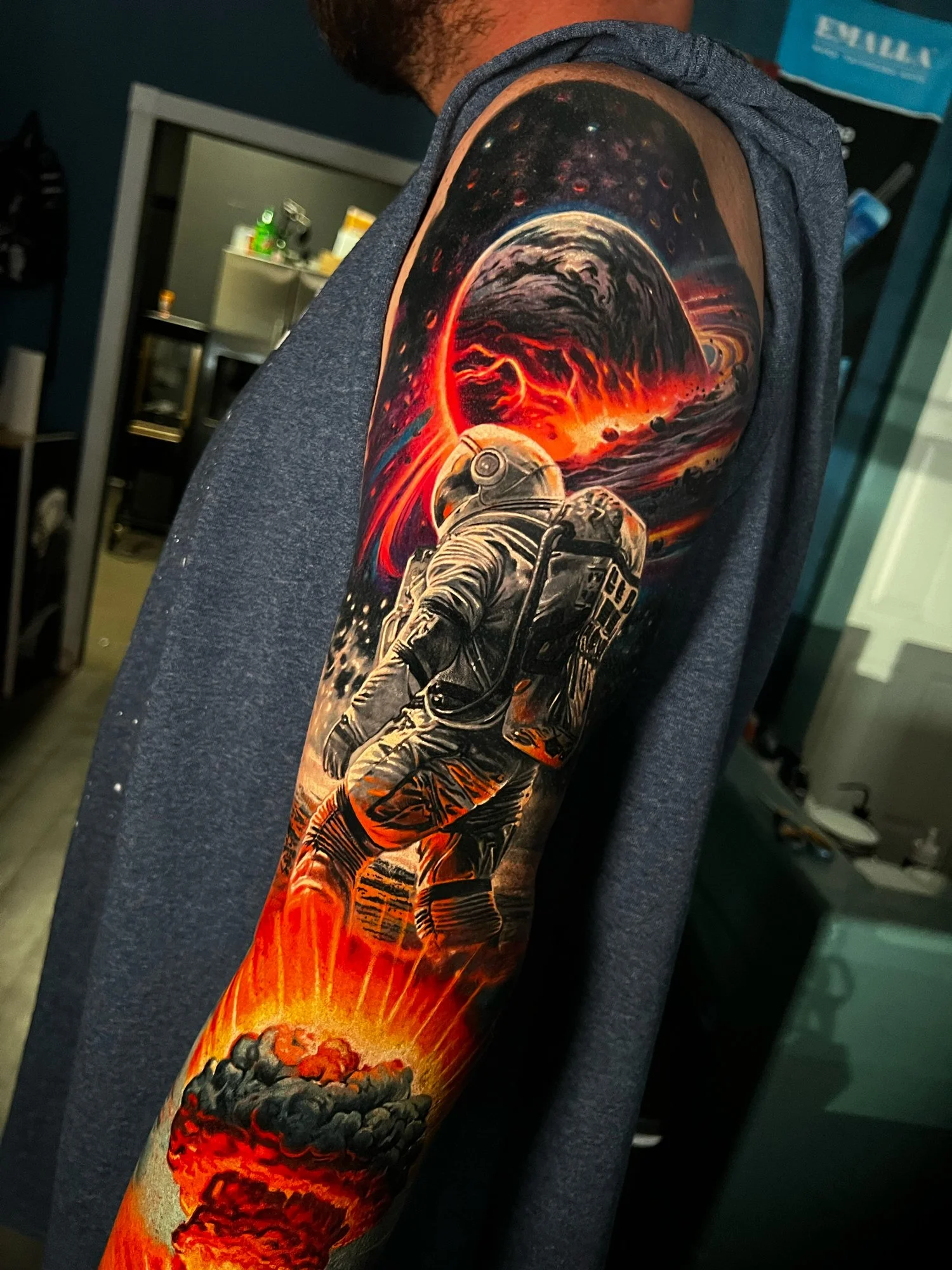 Tattoo of an astronaut in space with a fiery red and black planet and a volcanic eruption at the bottom on a person's upper arm.