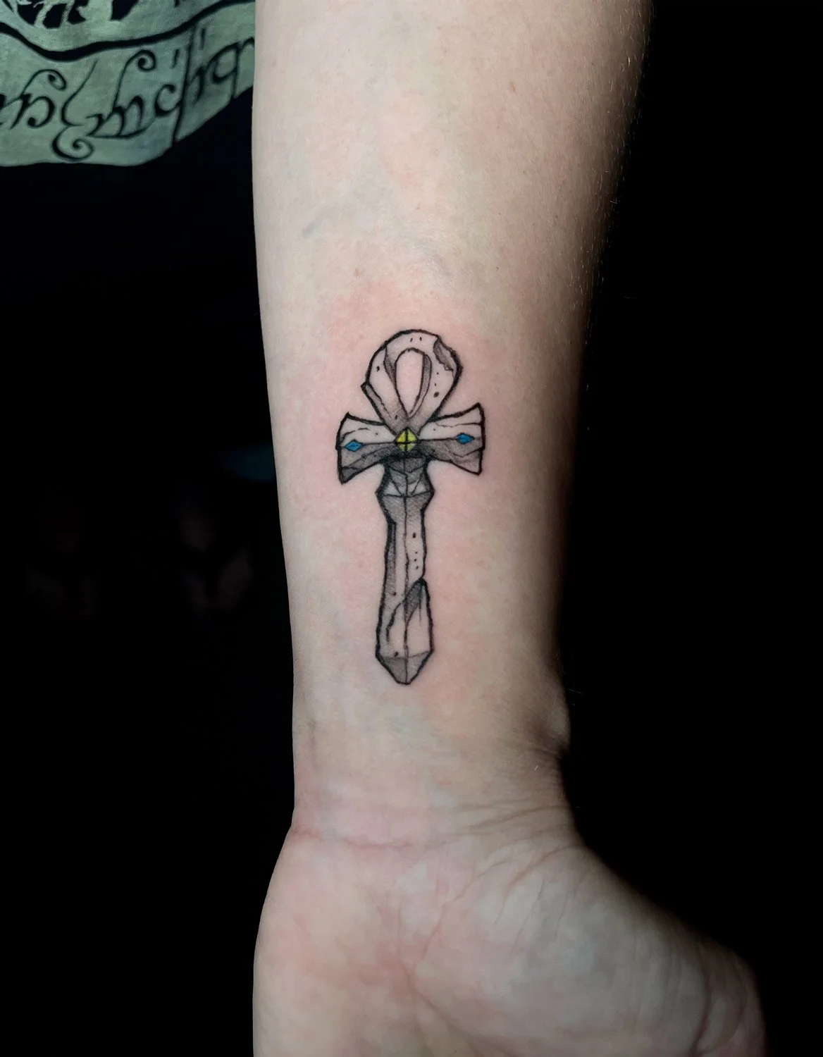 Tattoo of a geometric crystal sword with a bow tied around the hilt, on a person's forearm.