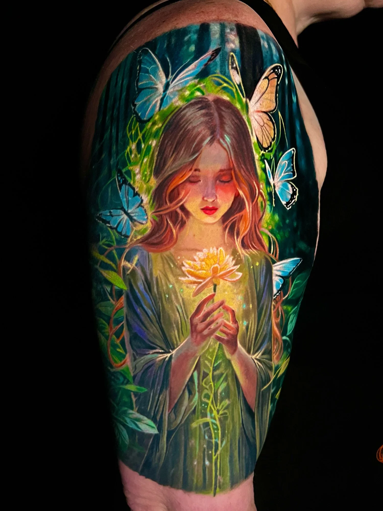 Tattoo of a girl with long hair holding a glowing flower, surrounded by colorful butterflies and greenery.