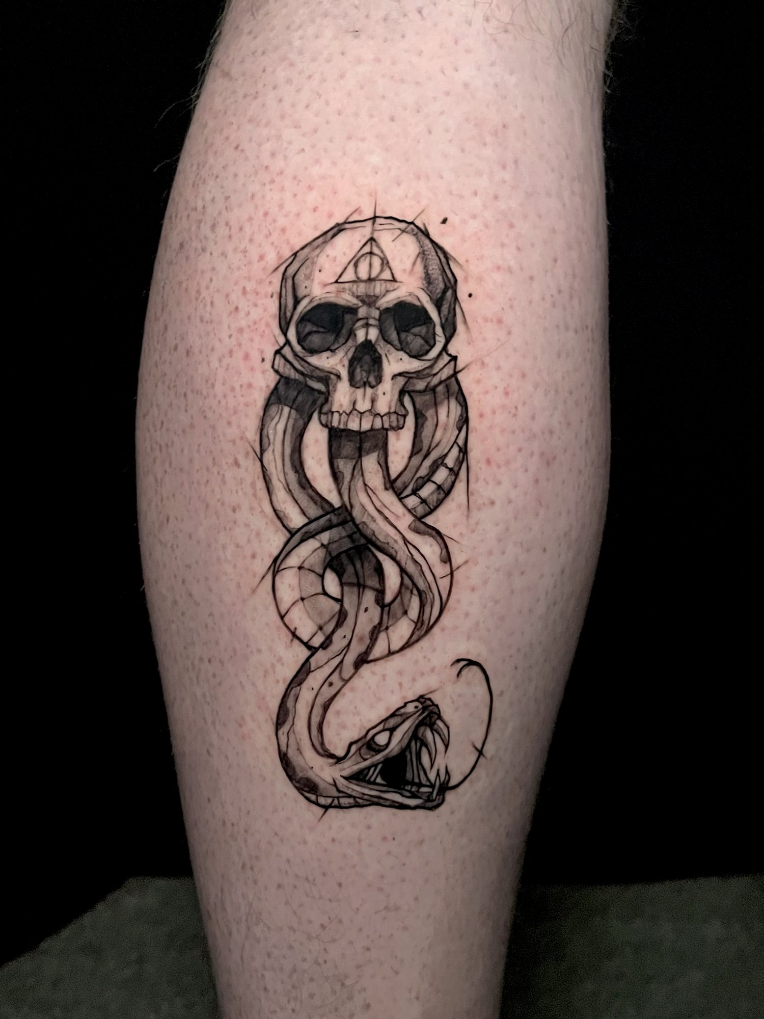 Tattoo of a skull with snake body on a person's leg.